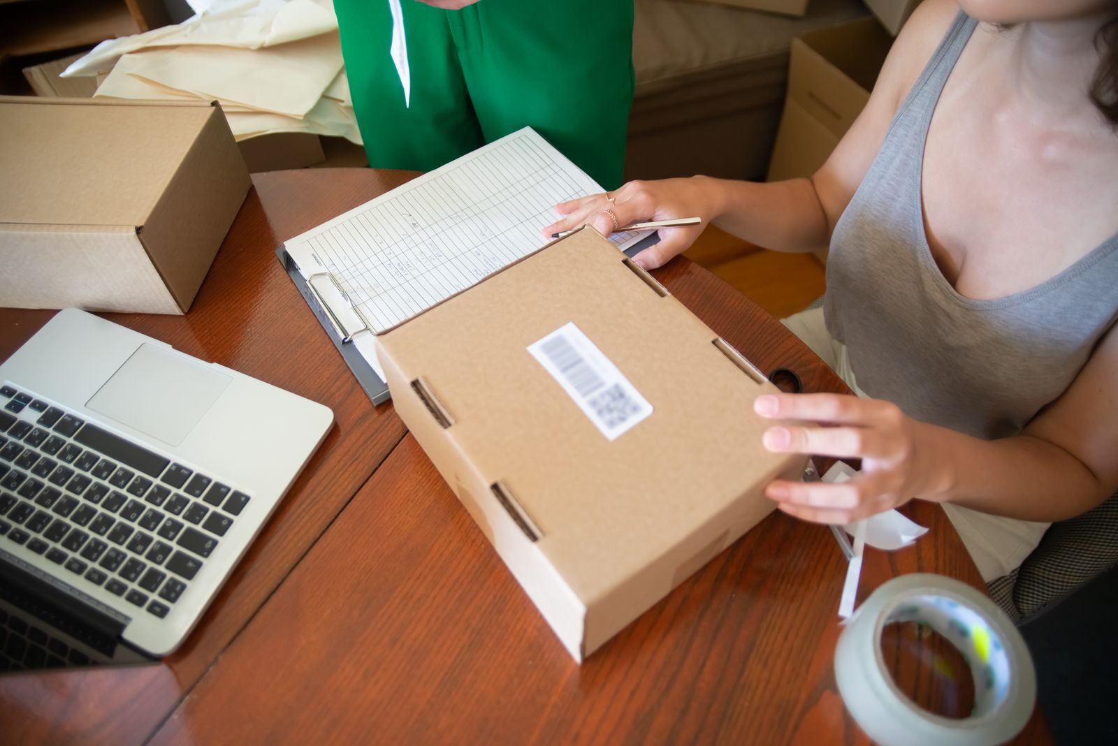 Online seller checking an order and packing a shipping box beside a laptop